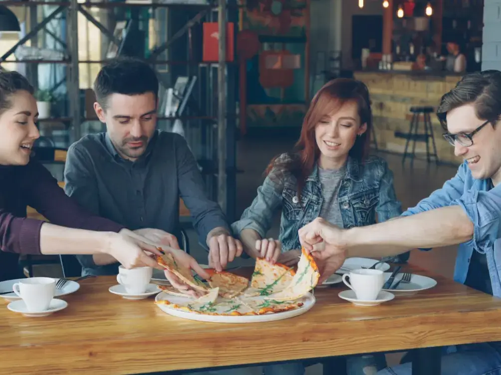 Four friends pulling slices from a pizza at a café table