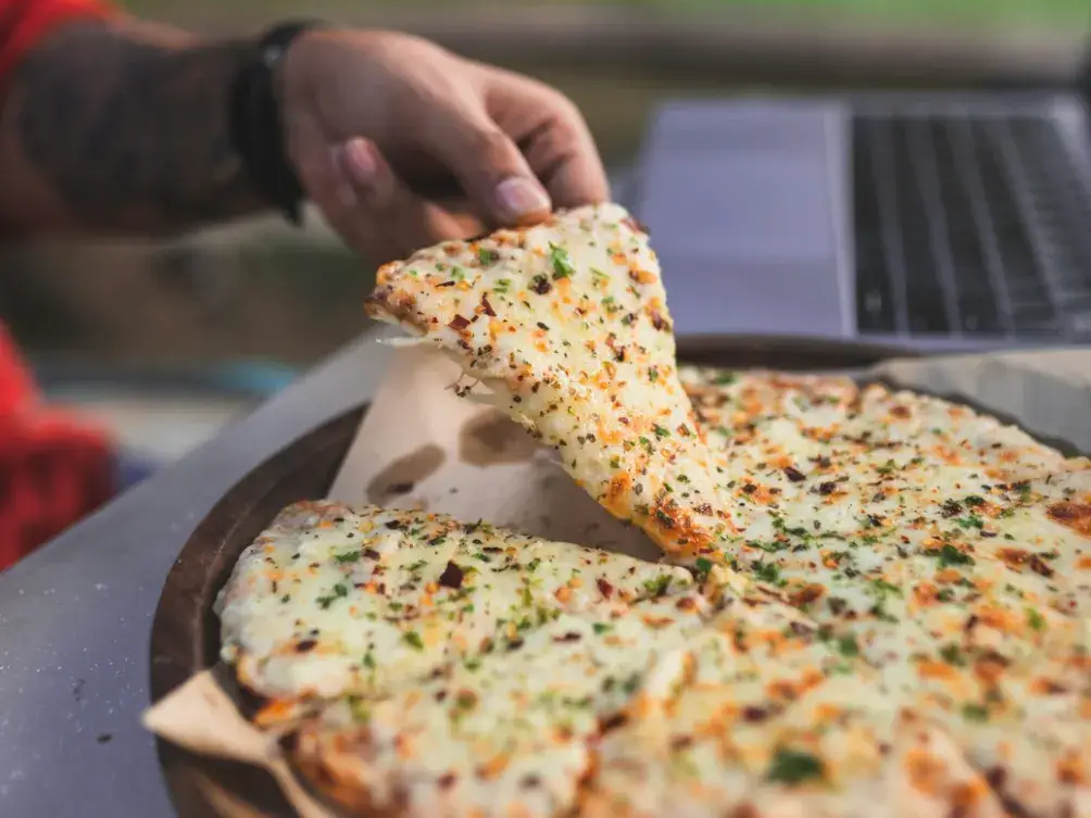 Taking a slice of pizza next to a laptop
